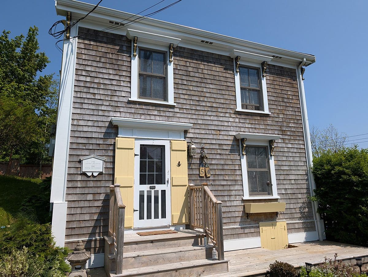 Two-story house with weathered cedar shingle siding, white trim, yellow shutters, and wood entry porch.